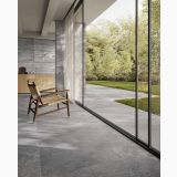 Gresie Bergstone Dark Antislip 120x120 cm – ambient living, terasa gri cu perete sticla, fotoliu lemn, gradina verde, pe pardoseala
