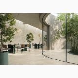 Gresie Origins Beige Mat 80x80 cm – ambient terasa, spatiu deschis cu pereti curbati, mese verzi si copaci, pe pardoseala